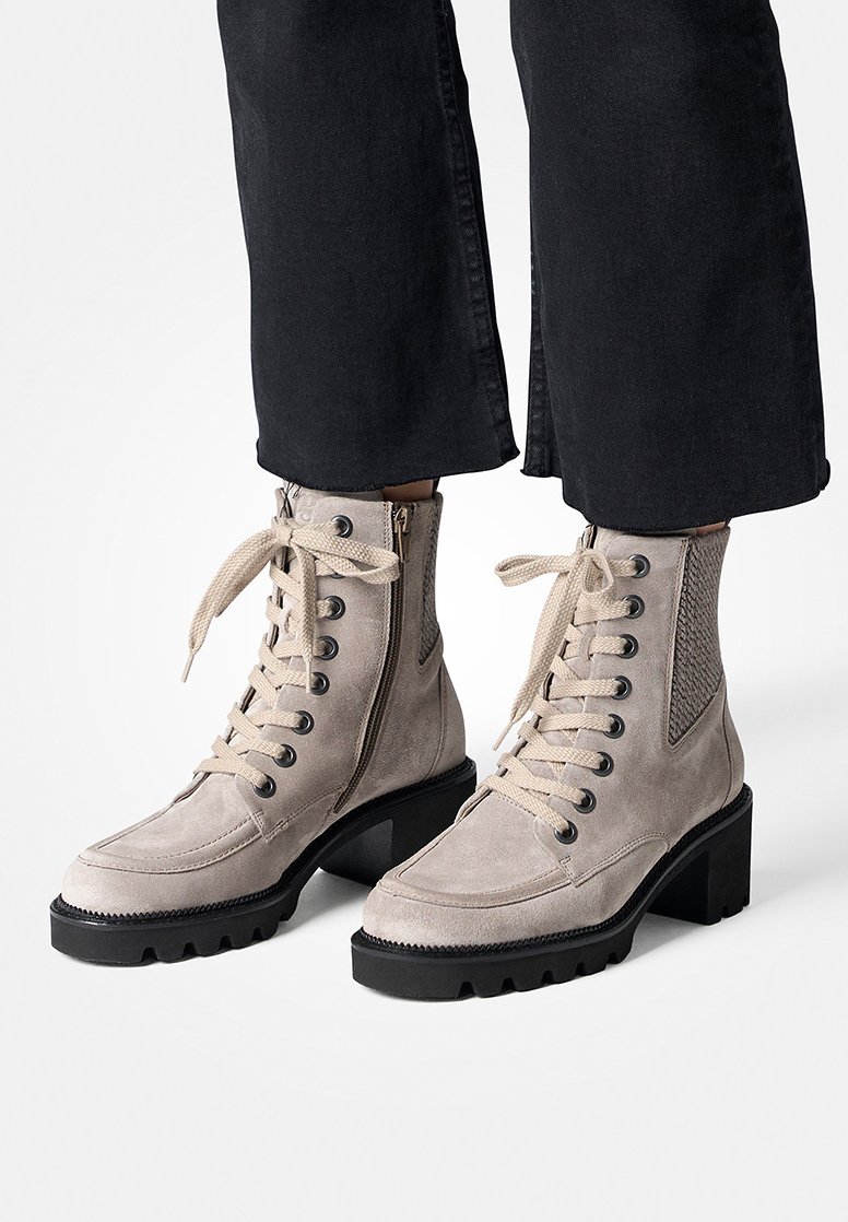 Bottines en suède beige avec une semelle épaisse noire, dotées d'une combinaison de lacets et de fermetures éclair, avec des détails en mesh sur les côtés.