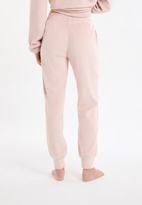 Pantalon de survêtement côtelé rose clair avec taille élastique, poches latérales et poignets fuselés, vu de dos. Texture douce, coupe décontractée.