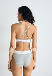 Sivi rebrasti set donjeg rublja s križnim trakama i trakama s Calvin Klein logotipom. Ima mekanu teksturu i minimalistički dizajn.
