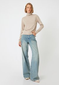 Pull en col roulé beige au design ajusté, associé à un jean évasé en denim léger bleu clair avec un léger délavage.