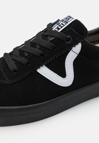 Baskets en daim noir avec lacets noirs, bande latérale ondulée blanche et semelle noire sur fond blanc.