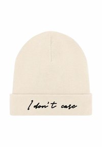 Cappello beanie in tessuto lavorato a maglia color crema; risvolto con testo nero che recita "Non mi interessa." Texture liscia, design senza cuciture, forma semplice.