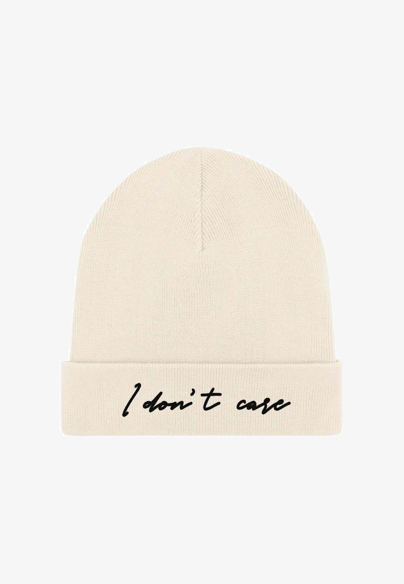 Cappello beanie in tessuto lavorato a maglia color crema; risvolto con testo nero che recita "Non mi interessa." Texture liscia, design senza cuciture, forma semplice.