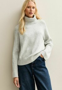 Jasnoszary sweter z golfem, z prążkowanymi mankietami i dolnym wykończeniem, zestawiony z ciemnoniebieskimi spodniami typu wide-leg. Miękka tekstura, swobodny krój.