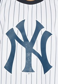 Maglietta da baseball bianca con righe navy, caratterizzata da un grande logo navy al centro. Il tessuto è testurizzato e traspirante.
