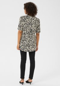 Blusa a maniche corte con motivo bianco e nero, orlo arrotondato, abbinata a jeans neri aderenti e sandali neri con tacco.