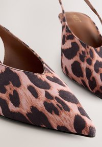 Coppia di scarpe slingback con punta a punta e motivo maculato marrone e nero su sfondo chiaro.