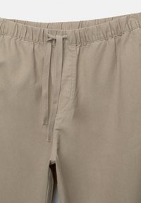 Beige katoen-stretch broek met een elastische tailleband en trekkoord. Voorzien van een enkele zak, een gladde textuur en een relaxte pasvorm.