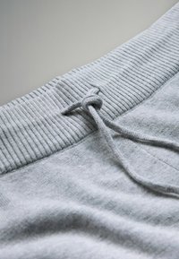 Tela de sudadera gris con una banda elástica acanalada en la cintura, con un detalle de cordón atado en el centro. Textura suave y lisa con un brillo sutil.