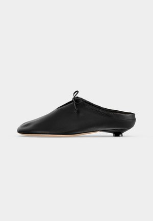 Μαύρο δερμάτινο mule χωρίς κούμπωμα με μικρό στρογγυλεμένο τακούνι και δεμένη λεπτομέρεια φιόγκου κοντά στο άνω άκρο, σε πλάγια όψη.