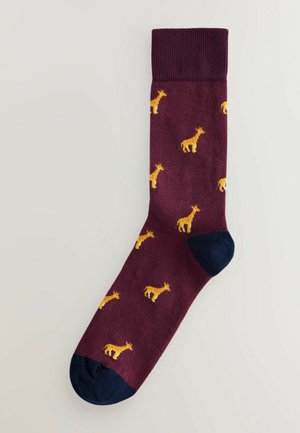 Bordeaux sokken met een patroon van kleine gele giraffen, met een donkerblauwe teen en hiel. Gestructureerde gebreide stof.