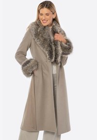 Béžový vlněný kabát s velkým límcem a manžetami z umělé kožešiny. Kabát má zapínání na jeden knoflík a A-liniovou siluetu.