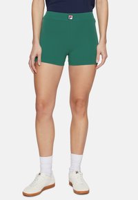 Gröna idrottsshorts med elastisk midja, med en logotypapplikation. Materialet är slätt med en tight passform. Bärs med vita sneakers och strumpor.