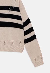 Strikkegenser i beige med svarte striper. Har en avslappet passform, ribbede mansjetter og detaljert søm i kanten og på ermene.