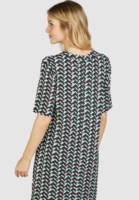 Kurzes Kleid aus schwarzem Stoff mit einem geometrischen Muster aus weißen, grünen und rosa Formen. Quadrat-Ausschnitt und lockere Passform.