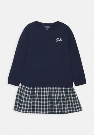 Marineblaues Kleid mit langen Ärmeln, bestickt mit dem "Polo"-Logo auf der Brust, und angenähtem schwarz-weiß kariertem Faltenrock.