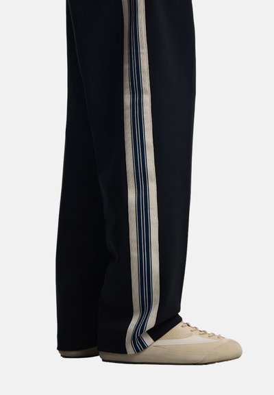 Mörkblå joggers med en bred sidopanel i krämfärgad och mörkblå rand. Sammanpassade med ljusbeige sportskor med texturerad ovandel.