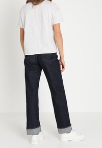 T-shirt grigio a maniche corte, jeans in denim scuri con risvolti, e sneakers bianche. Focus su un look casual, vestibilità rilassata e design semplice.