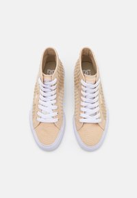 Beige Canvas-Sneaker mit einer strukturierten Seitenpartie, weißen Schnürsenkeln und Gummisohlen. Ausgestattet mit einem gepolsterten Kragen und einem Logo auf der Zunge.