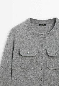 Cardigan en laine gris avec encolure ronde, fermeture à boutons sur le devant et deux poches à rabat boutonnées sur la poitrine.