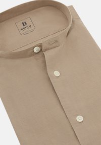 Camisa de Tencel beige con cuello abotonado, que presenta una etiqueta y tres botones en la parte delantera, textura suave y un diseño minimalista.