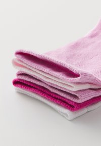 Kup stotih nogavic v različnih odtenkih roza in bele. Narejene so iz mehkega blaga z rebrasto teksturo. Vsaka nogavica ima zavit rob.