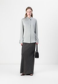 Ljusgrå knäppblus med krage, kombinerad med en mörkrandig maxikjol. Svart handväska och platta sandaler fulländar outfiten.