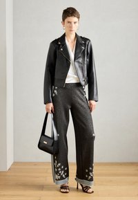 Personne portant une veste en cuir noire, un haut blanc, un pantalon large scintillant avec broderies florales, des sandales noires, et tenant un sac à main noir.