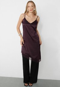 Vestido slip de satén burdeos con encaje en el bajo, con tirantes finos ajustables, combinado con pantalones negros de pierna ancha.