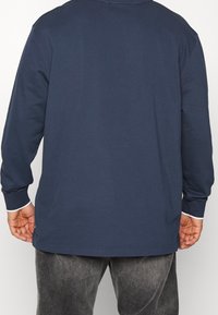 Marineblauw longsleeve t-shirt met een ronde hals, gemaakt van katoen, met witte accenten op de manchetten en de onderrand. Eenvoudig en onopgesmukt ontwerp.