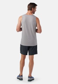 Herren leichtgraues, ärmelloses Sporttanktop mit strukturiertem Stoff, kombiniert mit dunklen Shorts und blauen Sportschuhen.
