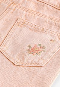 Tessuto di denim pesco con una tasca posteriore decorata da ricami floreali multicolori, che mettono in evidenza dettagli rosa e verdi in un motivo delicato.