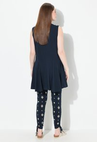 Tunica senza maniche blu navy con pieghe abbinata a leggings con motivi geometrici bianchi. Il modello indossa scarpe leggere e facili da indossare.