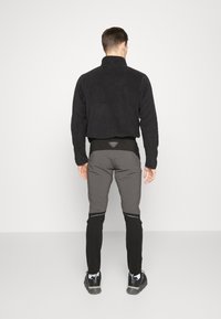 Black fleece jacket with a high collar, paired with two-tone fitted pants; grey upper and black lower sections, featuring reflective accents.