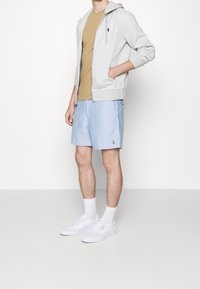 Grå zip-up hoodie, beige t-shirt, ljusblå shorts med logga, vita sneakers och ankelstrumpor. Avslappnad outfit med ledig passform och mjuka tyger.