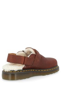 Bruine leren klomp met verstelbare band, pluche bontvoering, ronde neus en gele stitching op een dikke, gestructureerde zool.