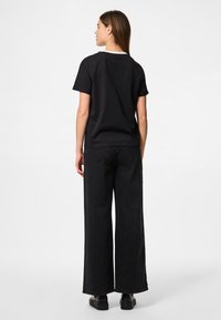 Must have musta T-särk lühikeste varrukatega, koos avara musta denimpüksiga. Sile tekstuur, minimaalne disain, ilma nähtavate mustrite või aktsentideta.