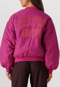 Fuchsia bomberjacket met oversized mouwen, geribbelde manchetten en de tekst "HARPER AND YVE" in vet oranje op de rug.