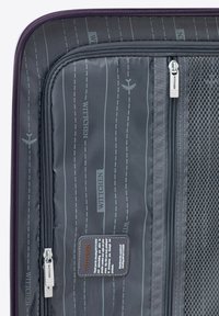 Gray interior of a suitcase with mesh pocket, multiple zippers, and printed airplane and text patterns. Features a "WITTCHEN" tag.