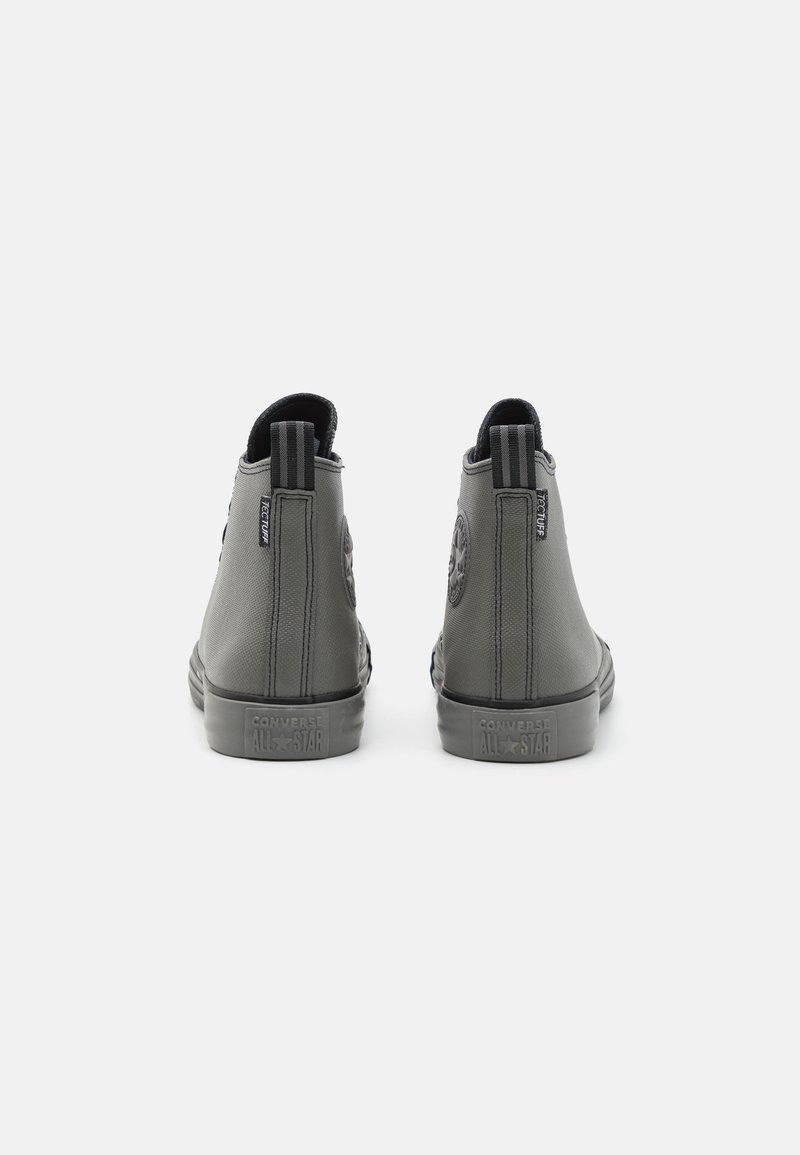 Scarpe alte grigie con materiale sintetico liscio, dettagli testurizzati e iconiche etichette sul retro e sul lato. Design con suola piatta.