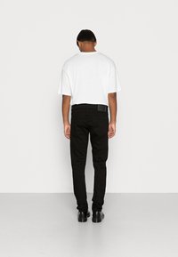 Svarta slim fit jeans och en vit oversized t-shirt, sedd från baksidan. Jeansen har en lapp på midjebandet. Slitstark, avslappnad tyg.