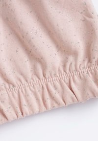 Un tissu rose clair présente des points de paillettes argentées dispersés. L'ourlet a une texture froncée, créant une apparence douce et élastique.