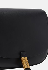 Borsa a tracolla in pelle nera caratterizzata da una forma arrotondata, una texture liscia e una chiusura dorata con il nome del marchio "PINKO" impresso.