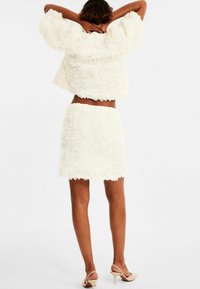 Vit blommig texturerad kort jacka och matchande kjol. Outfiten har en mjuk, lager-på-lager design med scallop-kant. Tillbehör inkluderar klackskor.