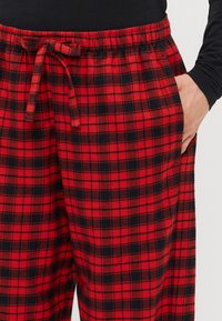 Rød og sort rutet flannel pyjamabukser med elastisk talje og snøre, der har sidelommer og en blød tekstur.