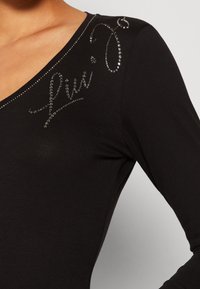 Top nero a maniche lunghe con scollatura a V, caratterizzato da strass decorativi disposti in un motivo corsivo sulla spalla sinistra.