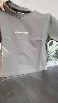 Šedé tričko s krátkým rukávem z hladké tkaniny, na přední straně se středovým bílým logem "PEGADOR". Minimalistický design s kulatým výstřihem.