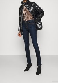 Svart, glänsande puffjacka med hög krage, leopardmönstrad långärmad topp, mörkblå tajta jeans och svarta ankelboots med spetsig tå.