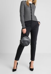 Svart mönstrad knäpp upp cardigan med diamantdesign, ihopparad med skräddarsydda svarta byxor och en rund svart handväska. Högklackade skor.