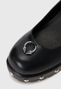 Black leather shoe featuring a rounded toe, silver spike accents, and studs on the sole. Textured interior with minimal design.